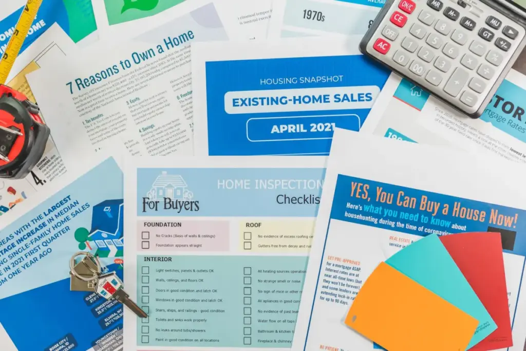 Vista de cima de folhetos imobiliários, listas de verificação e uma calculadora para compra de imóvel.