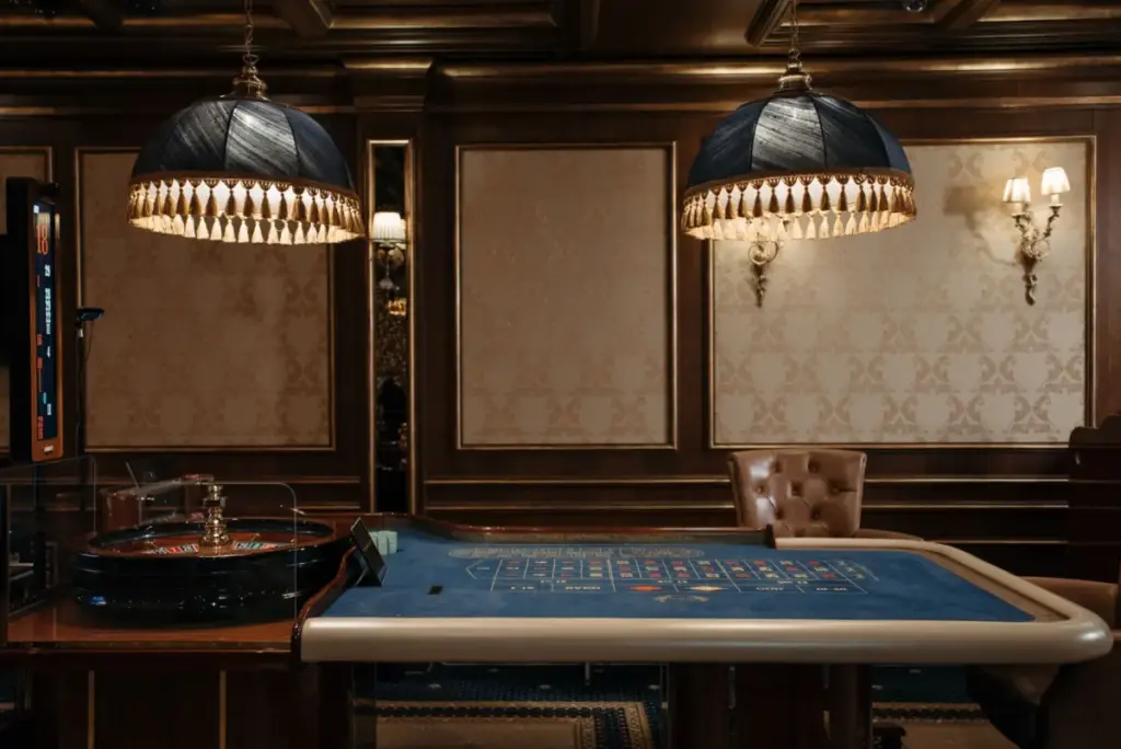 Interior luxuoso de cassino com uma mesa de roleta tradicional sob luminárias elegantes.