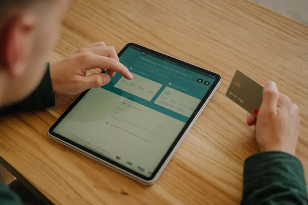 Pessoa fazendo um pagamento online usando um tablet e um cartão de crédito em uma mesa de madeira.