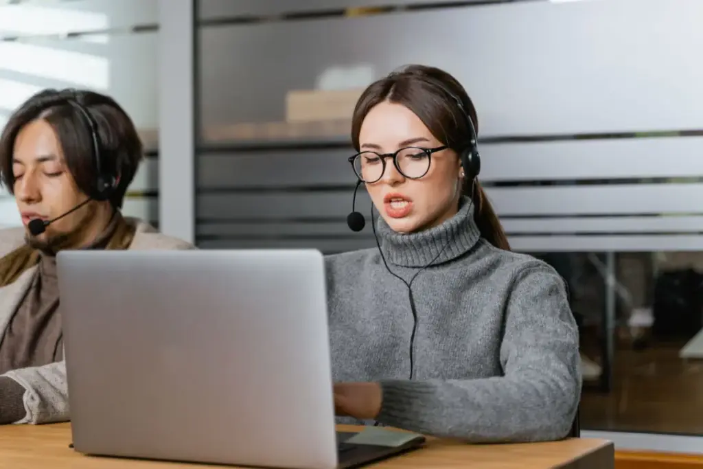 Atendentes de suporte ao cliente usando headsets trabalhando em notebooks em um escritório moderno.
