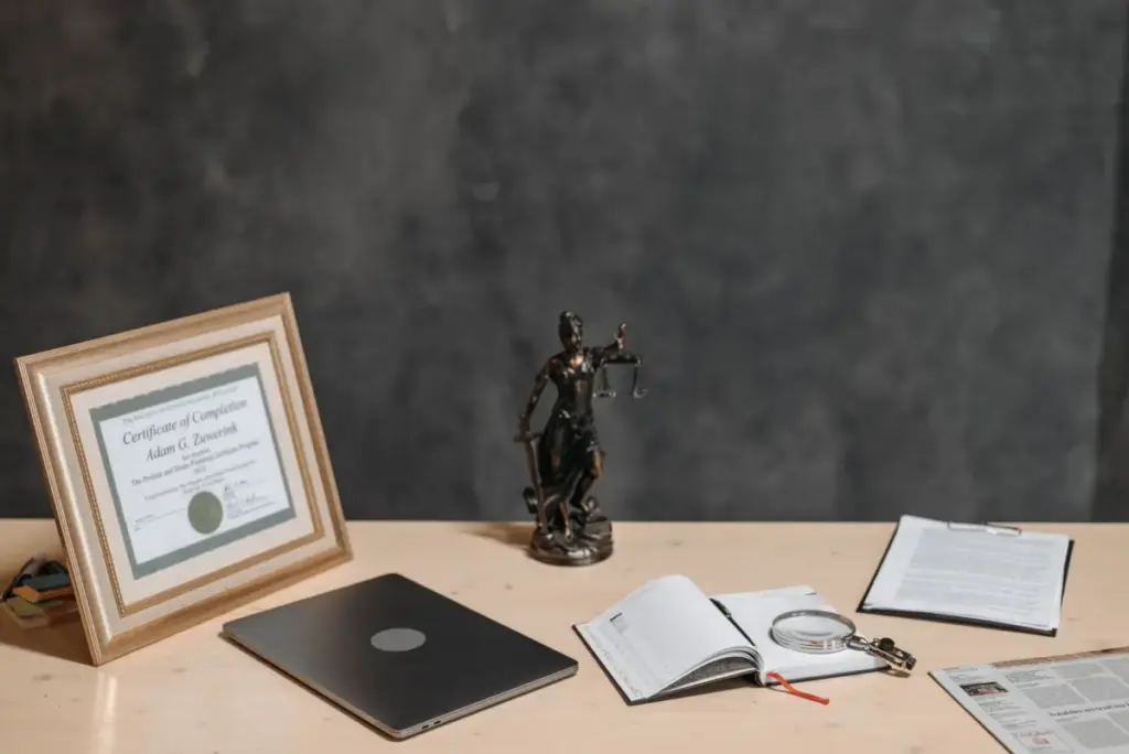 Mesa de advogado com estátua da justiça, diploma, laptop, lupa e documentos.