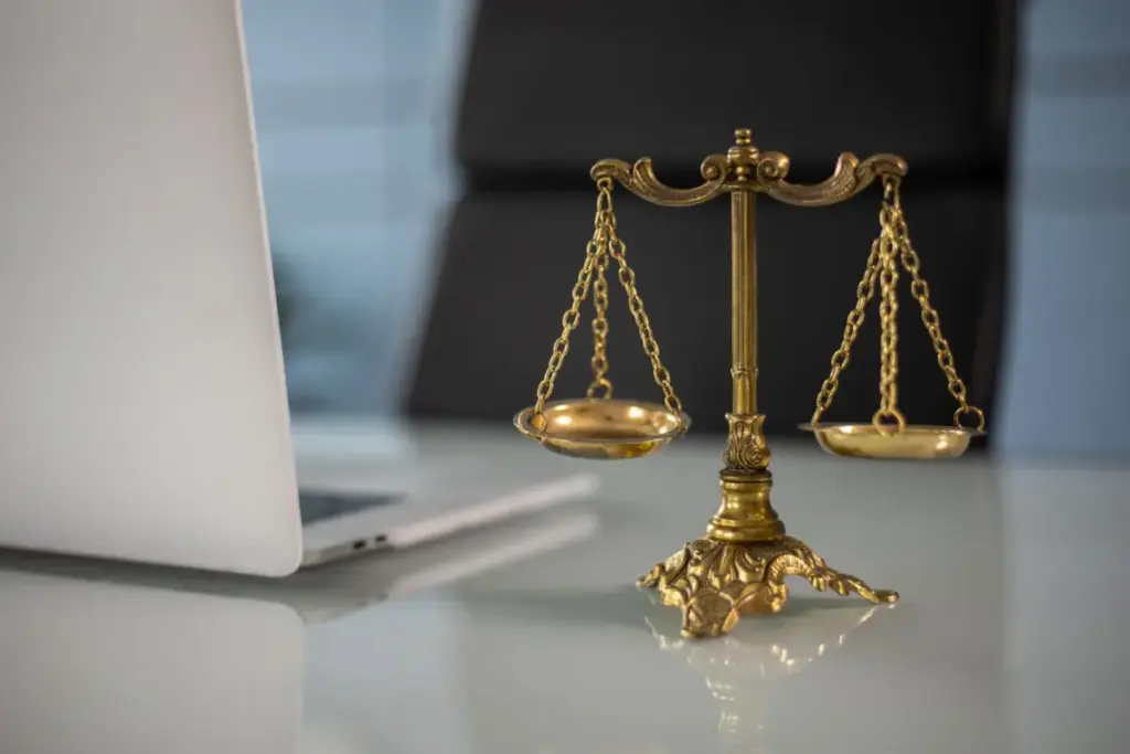 Balança da justiça dourada sobre uma mesa ao lado de um laptop, simbolizando lei e equilíbrio.