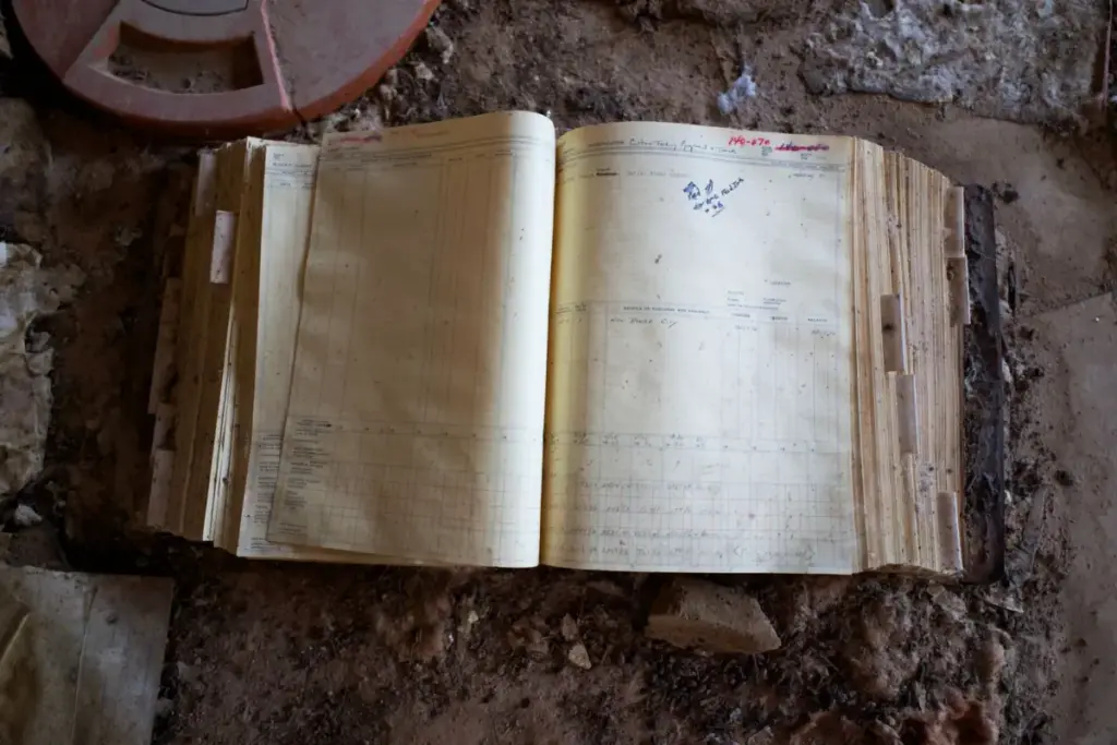 Um livro-razão aberto em um piso empoeirado, evocando uma sensação de história e abandono.