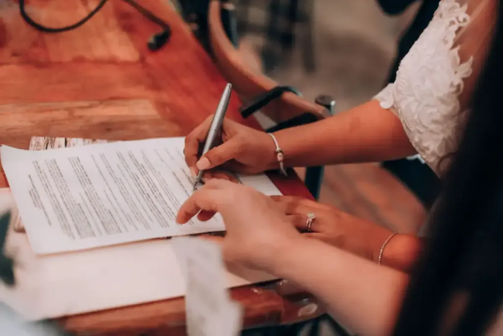 Mãos assinando um documento importante em uma mesa de madeira, simbolizando acordo e compromisso.