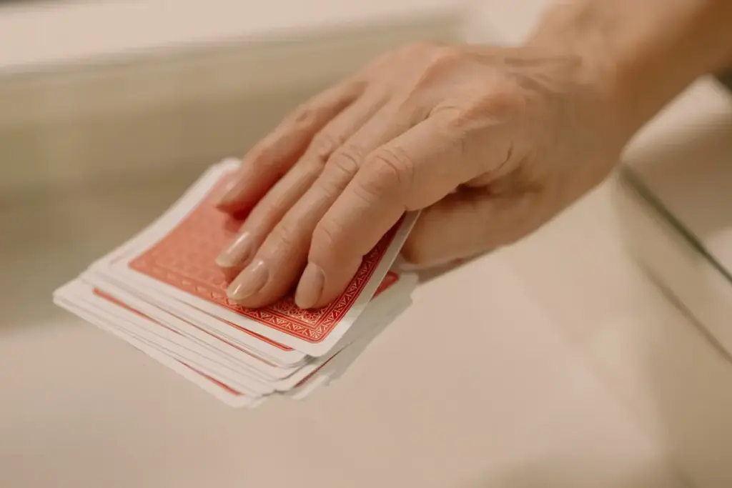Mão selecionando cartas do baralho sobre mesa de vidro reflete um tema lúdico e recreativo.