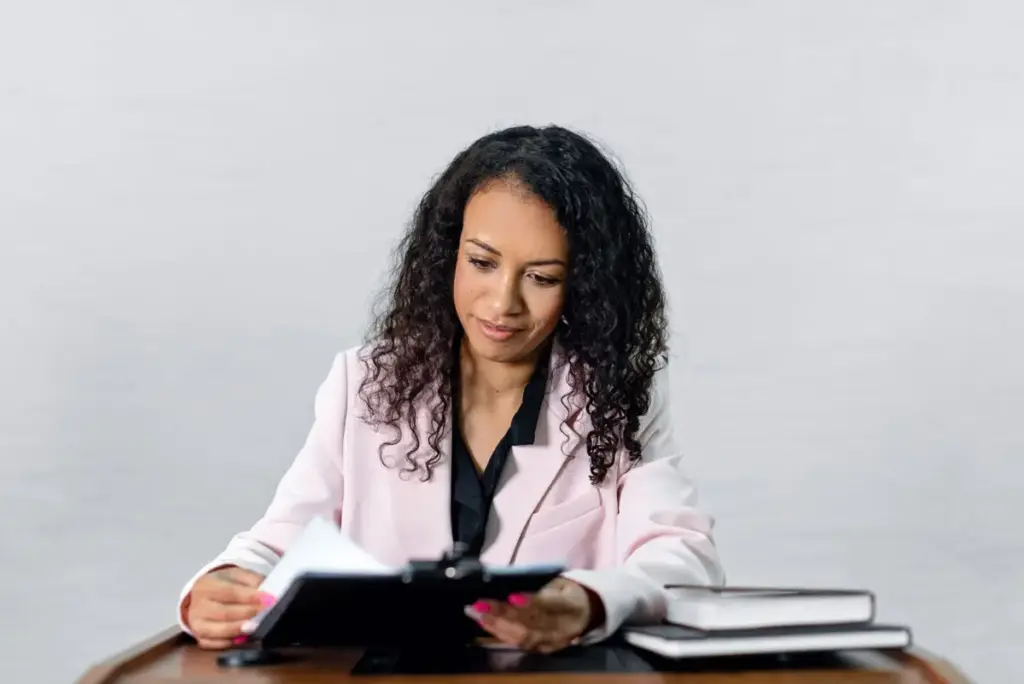 Mulher confiante com cabelo cacheado em traje formal revisando documentos em uma mesa.